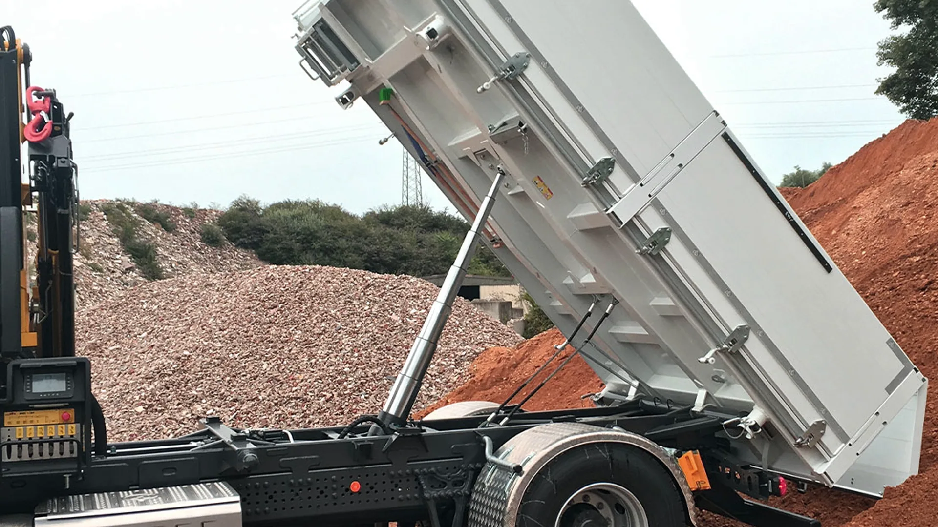 Multi-stage underbody cylinder tipping a dump trailer body while unloading aggregate